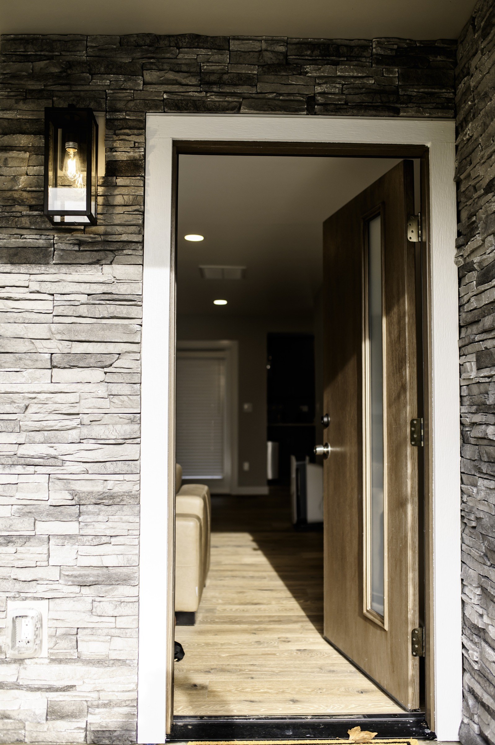 Open wood entry door framed by sidelights and stone cladding