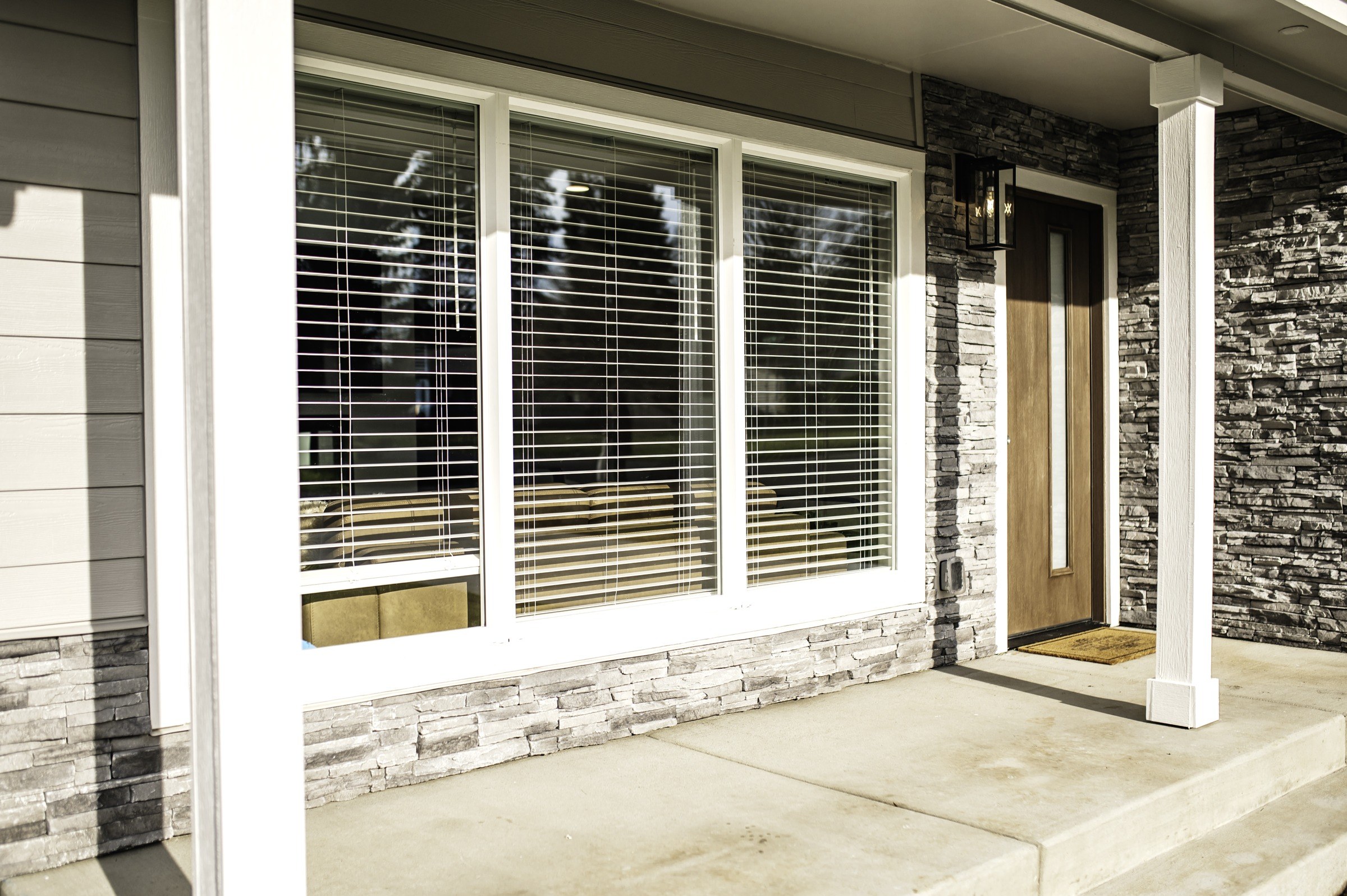 Covered front porch with wood entry door, windows and stone cladding