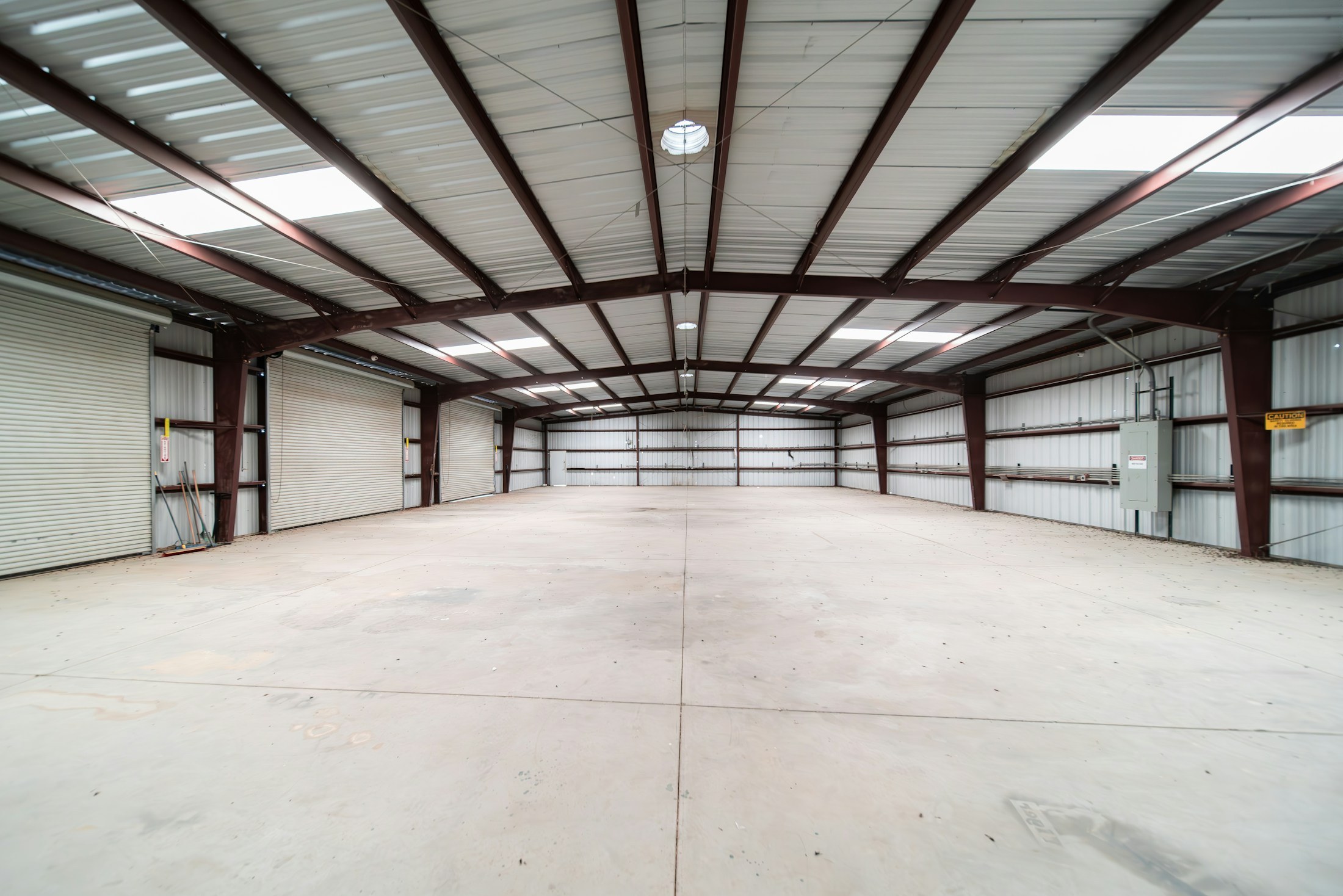Empty steel-framed warehouse with roof lights and rolling doors.