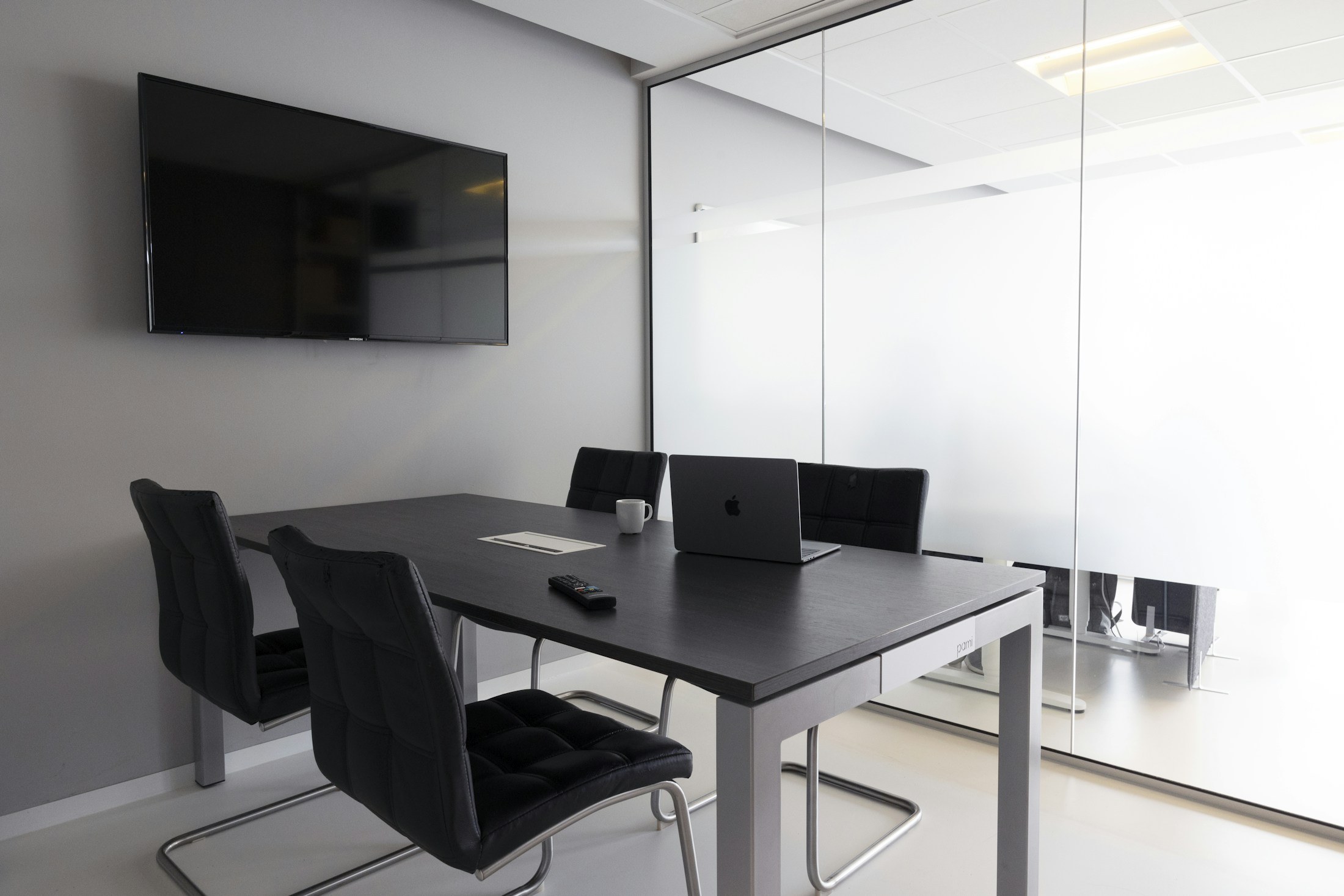 Compact gray meeting room with a glazed partition and wall-mounted screen.