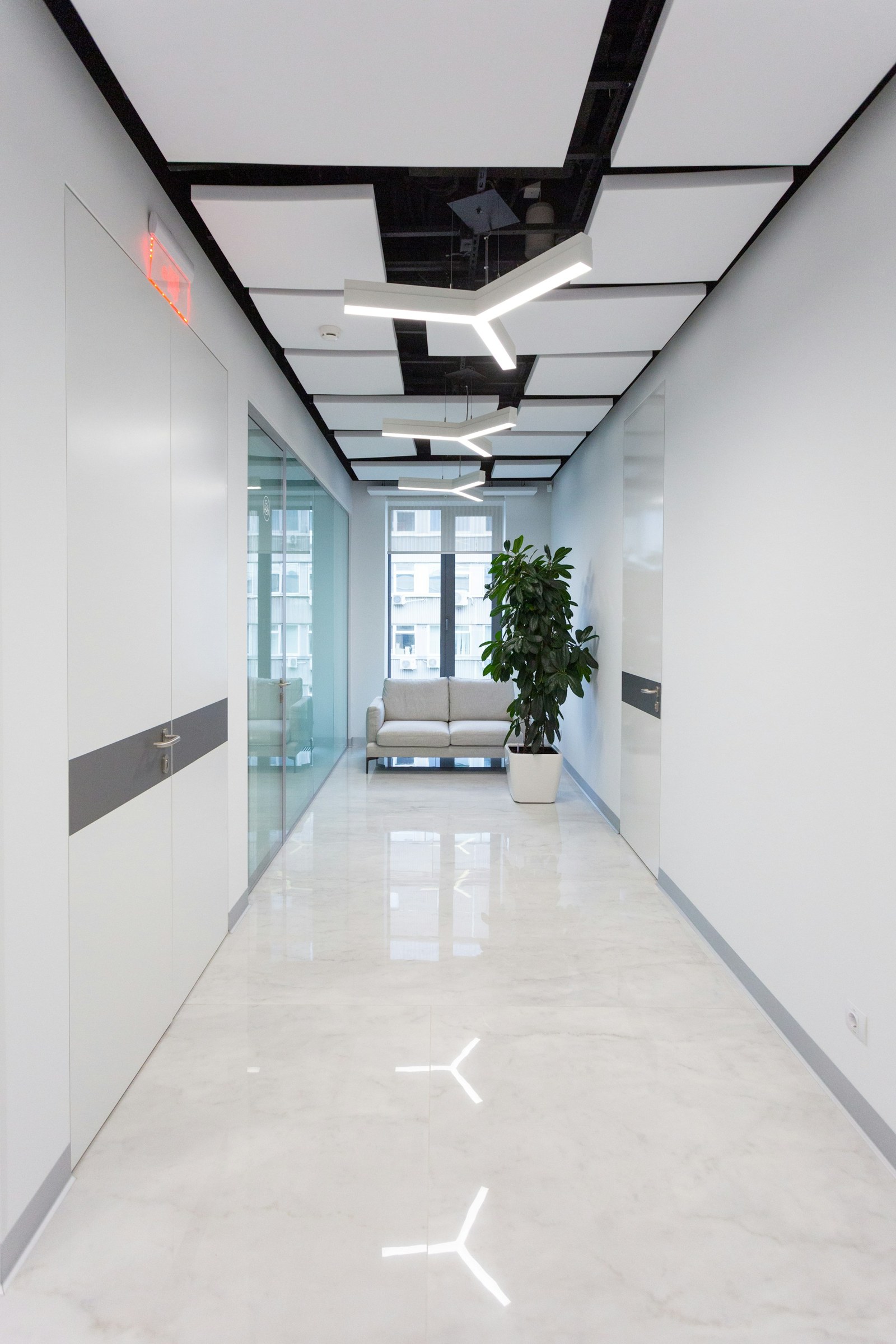 Office corridor with glass doors and geometric ceiling lighting.