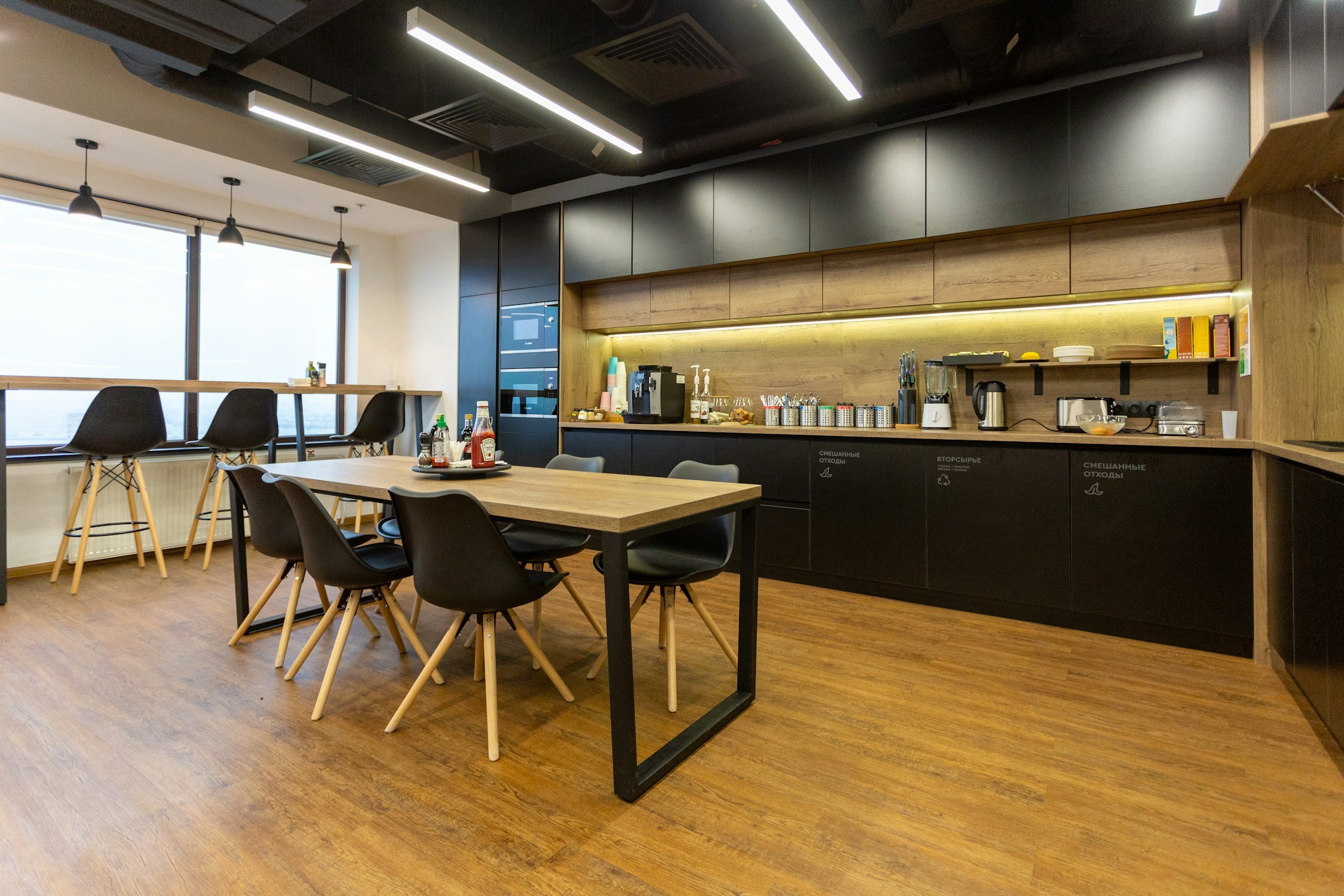 Office breakroom with timber cabinetry beneath an exposed dark ceiling.