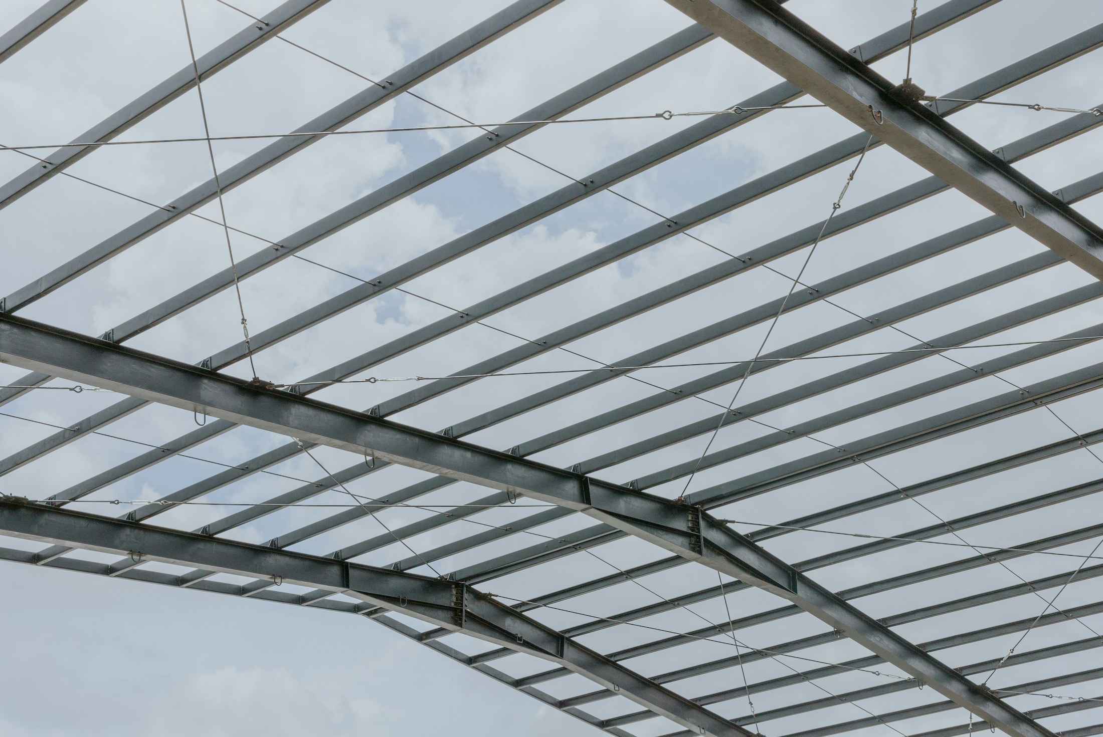 Exposed steel roof framing against a cloudy sky.