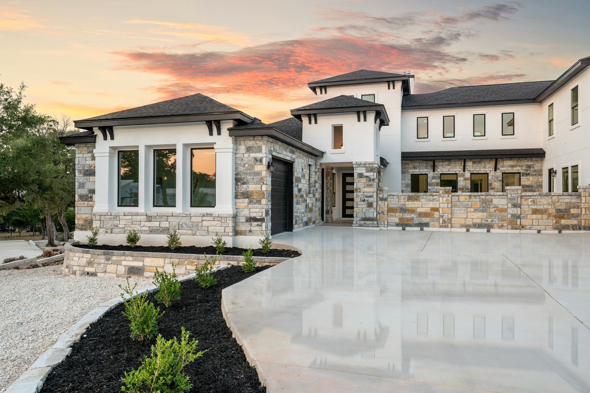 Contemporary two-story home with stone accents, a garage and broad driveway at sunset