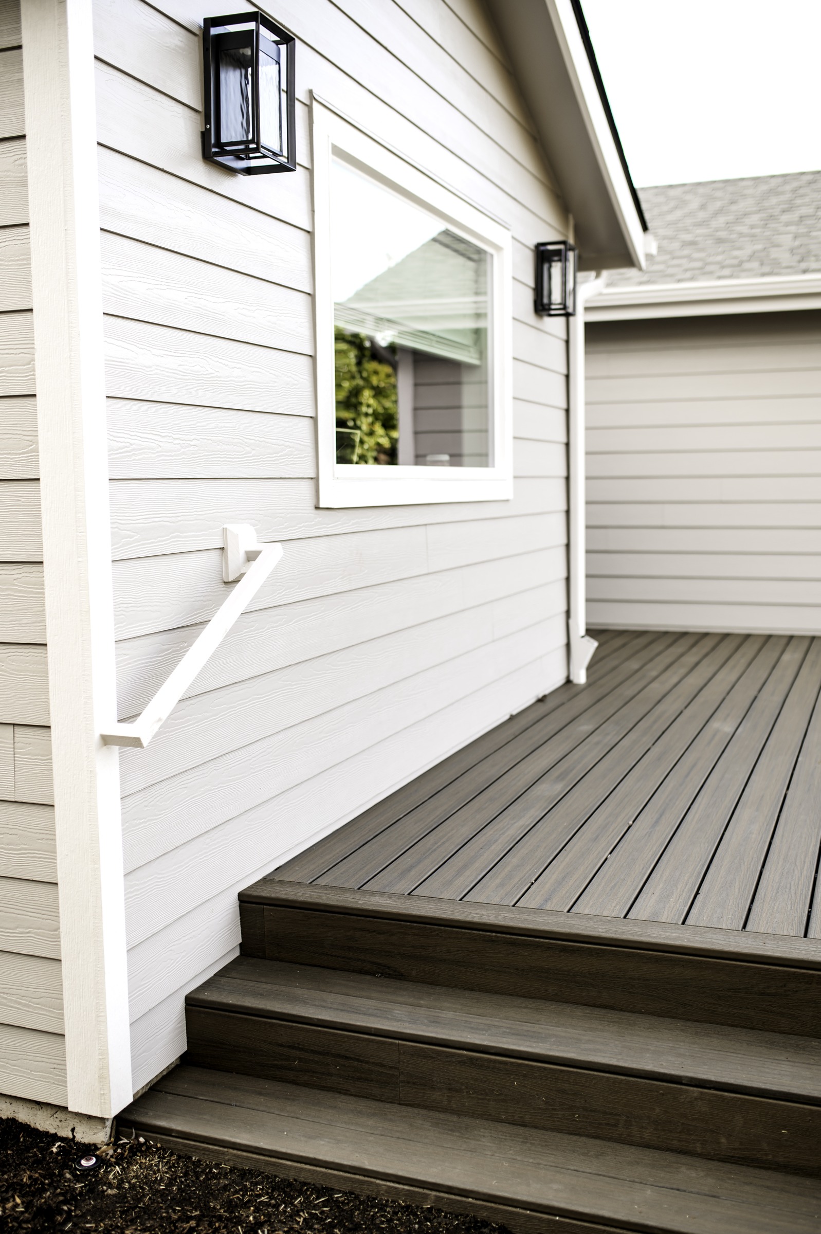 Light lap siding, white window trim and black lanterns beside deck steps
