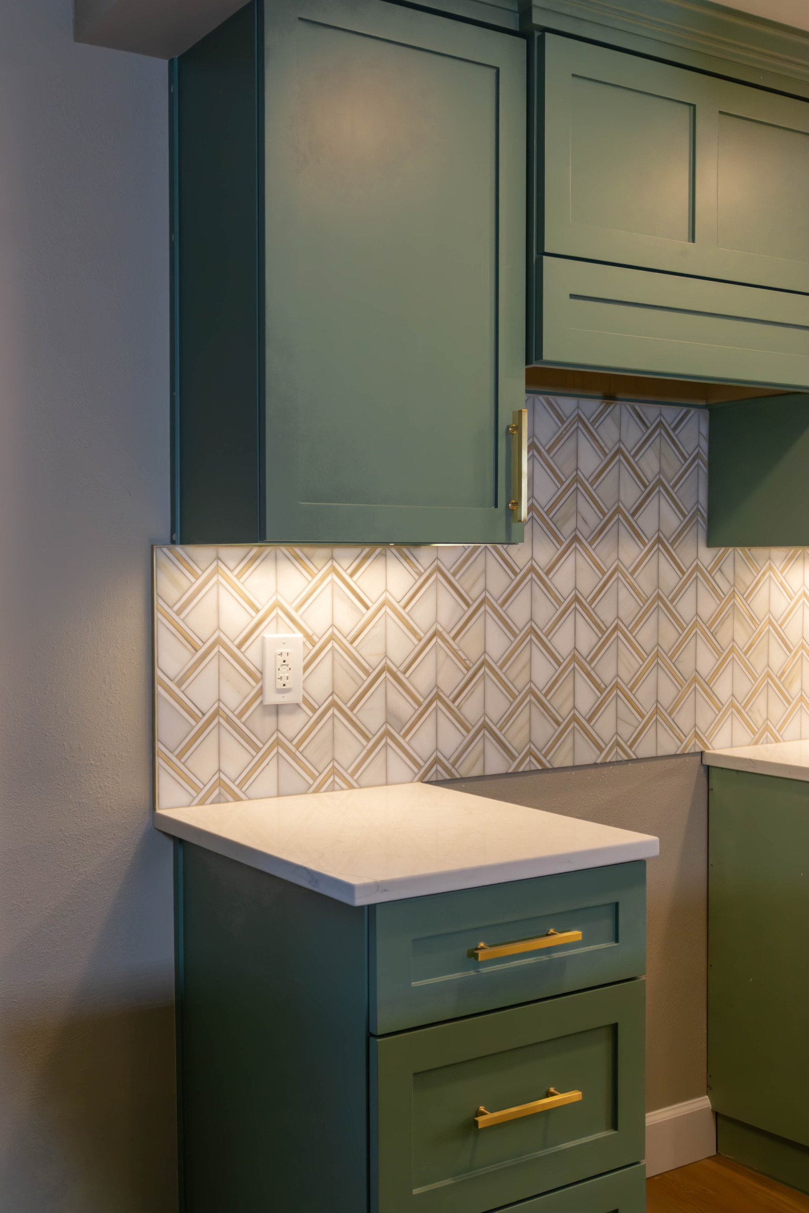 Green drawers and wall cabinetry with brass-toned hardware and patterned backsplash