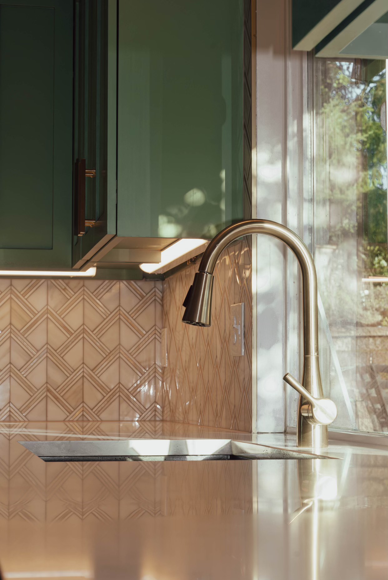Brass-toned kitchen faucet, pale countertop, and green cabinetry