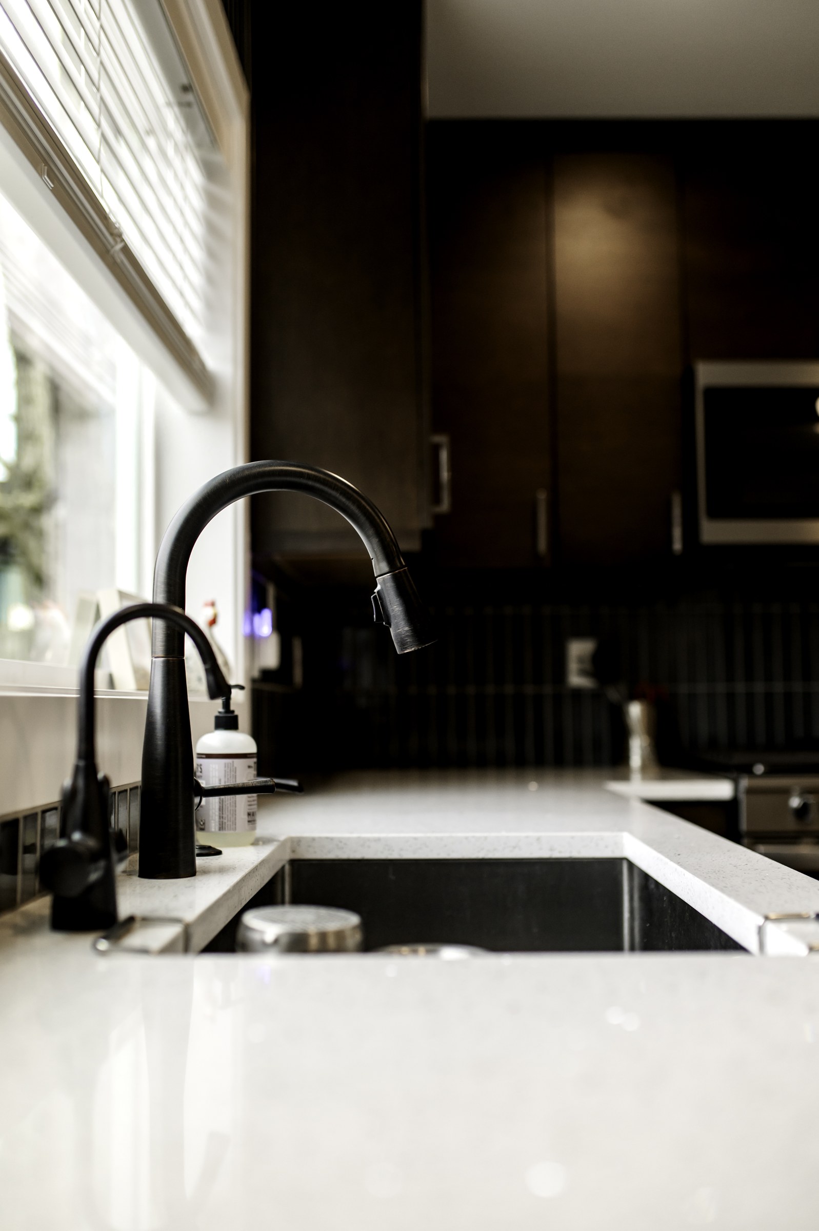 Resolution kitchen detail with a dark faucet, undermount sink, light countertop, and dark cabinetry
