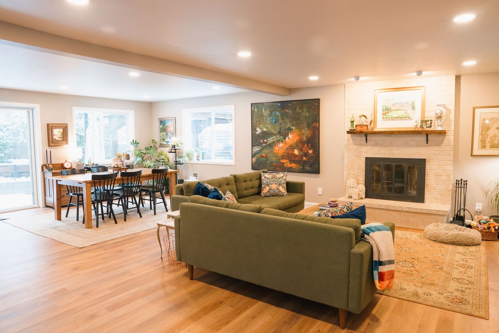 Open living and dining room with wood flooring, broad windows and a fireplace at the far end