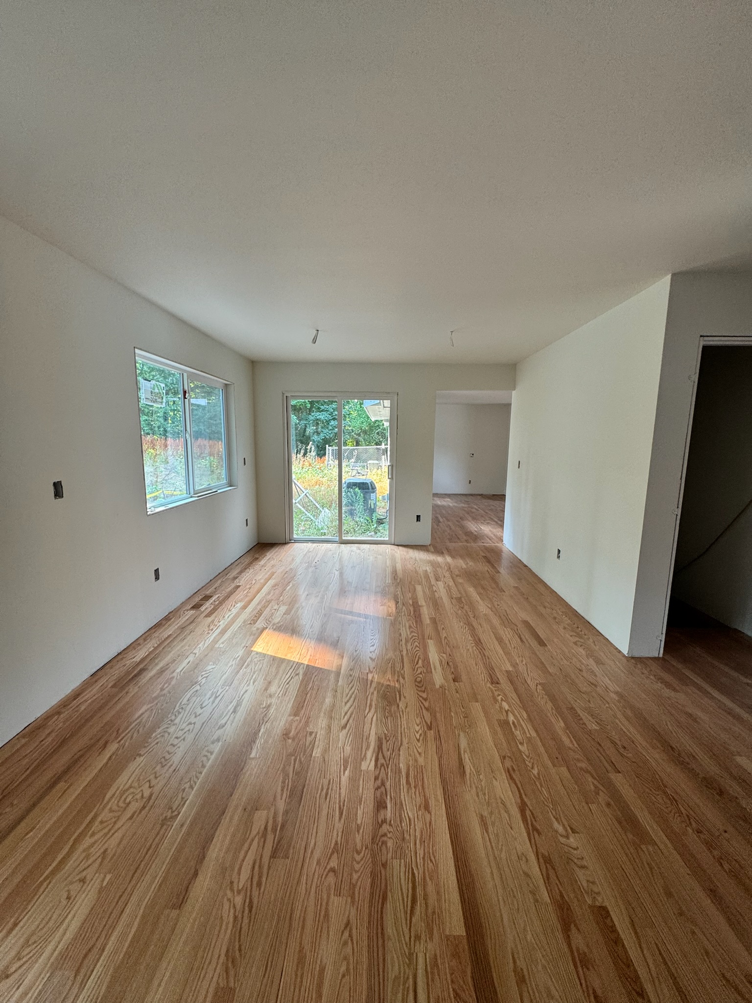 Room during reconstruction with wood flooring, painted walls, unfinished trim and electrical openings.