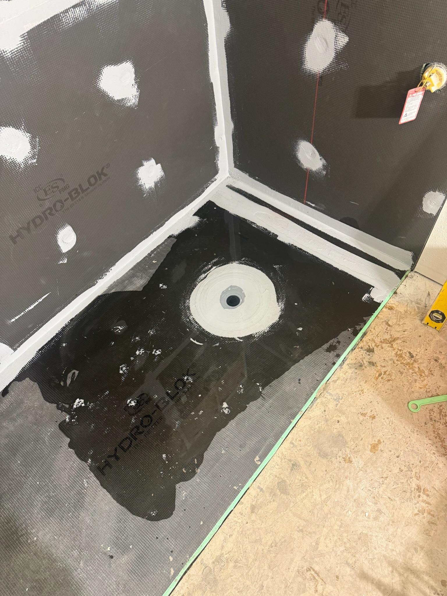 Shower base and wall backer panels with sealed joints and an exposed drain before tile installation.