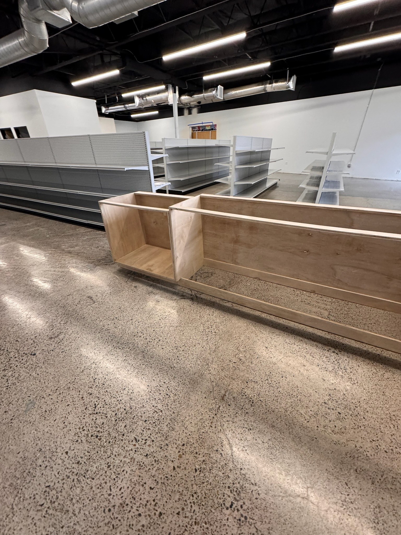 Counter cabinetry during installation beside retail shelving and exposed overhead services.