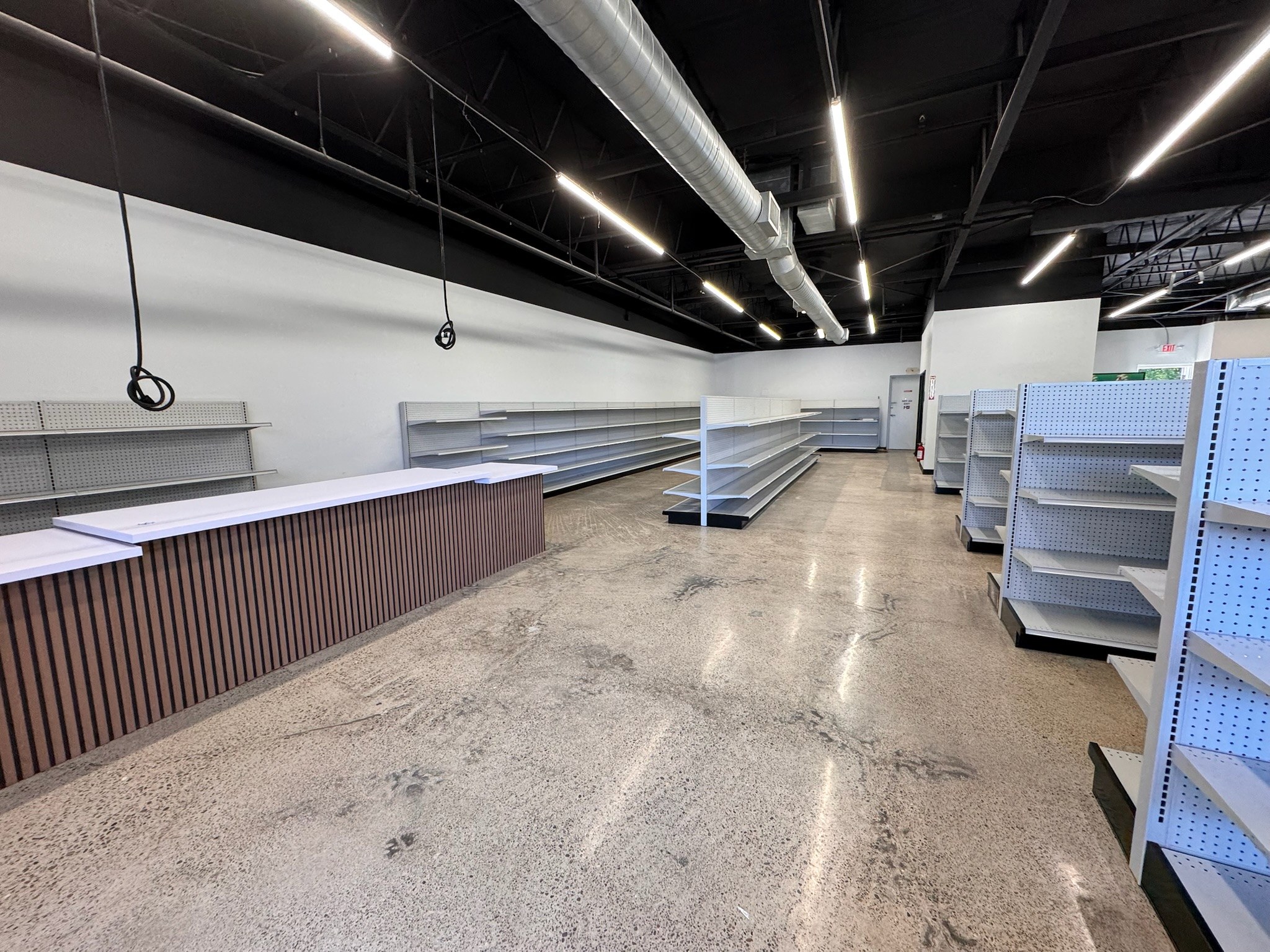 Retail fit-out with a slatted counter, shelving, exposed dark ceiling, ductwork and linear lighting.