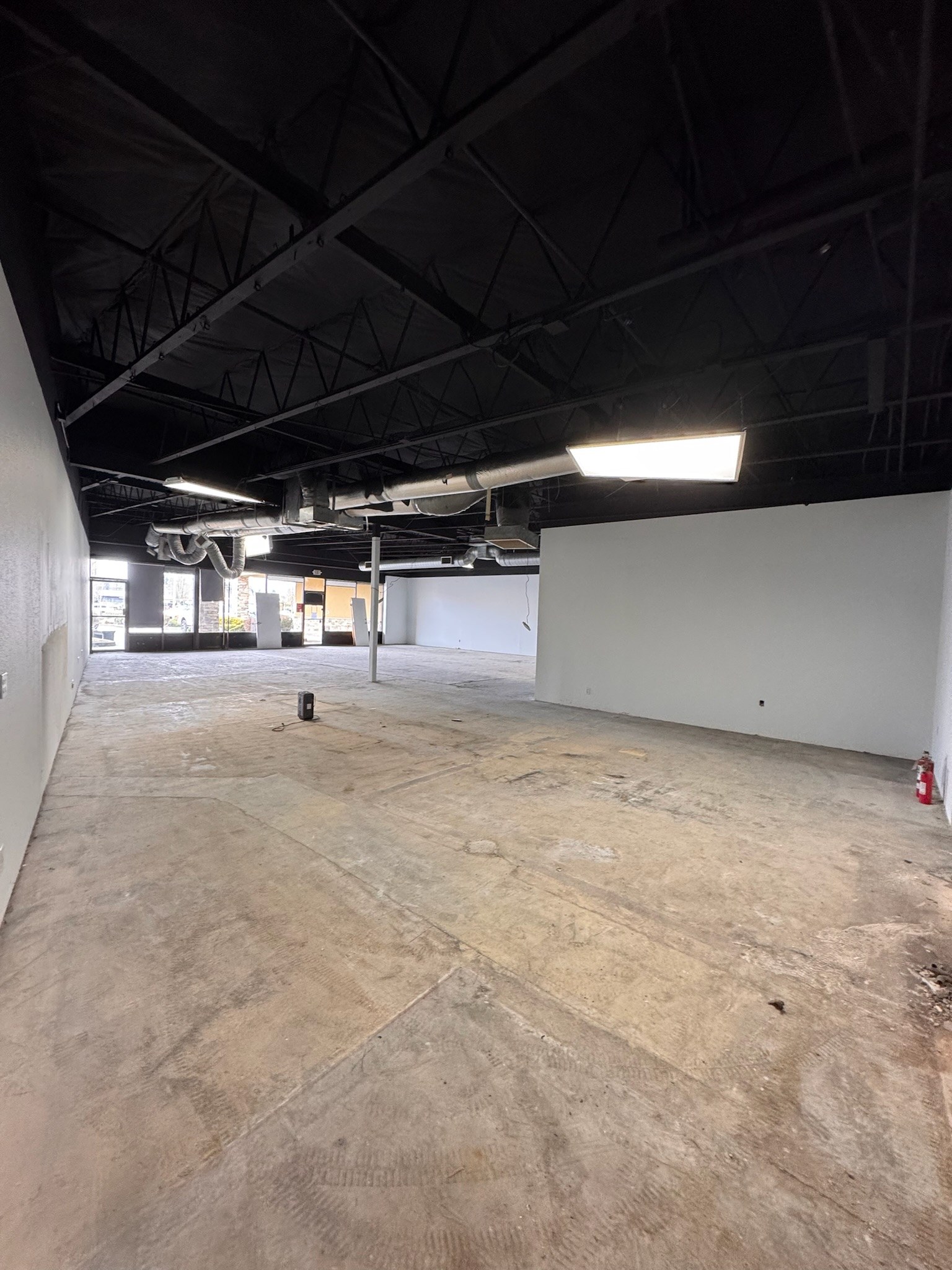 Retail interior before fit-out, with an exposed dark ceiling, white walls and an open concrete floor.