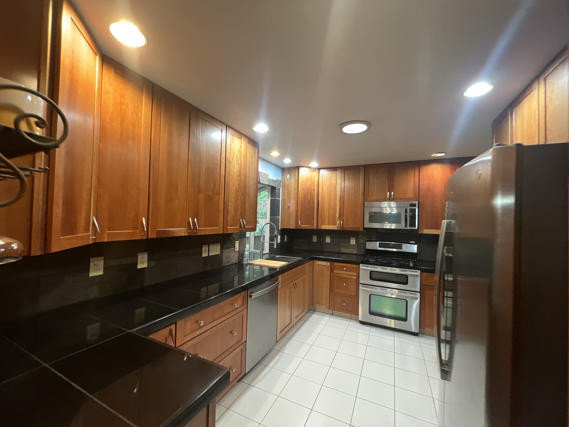 Wood kitchen cabinetry with dark counters and light tiled flooring
